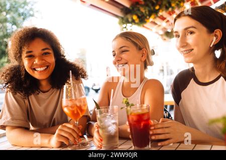 Nahaufnahme von drei charmanten Mädchen, die in einem Café gekühlte Cocktails trinken. Gläser mit leckeren Fruchtgetränken und Eiswürfeln. Lächelnde Freunde entspannen sich und dr. Stockfoto