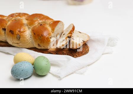 Geschnittenes osterbrot auf Holzteller auf weißem Tisch mit bunten ostereiern Stockfoto
