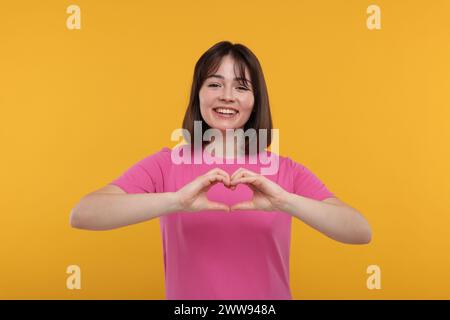 Glückliche Frau, die Herzgeste mit Händen auf orangefarbenem Hintergrund zeigt Stockfoto