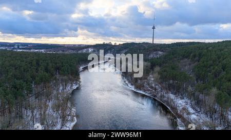 Drohnenfotografie des Flusses, der durch Park, Wald und Stadt fließt, am Horizont während des Winters Stockfoto