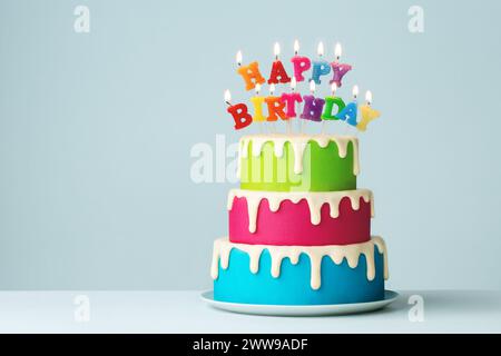 Farbenfrohe, gestufte Geburtstagskuchen mit bunten Geburtstagskerzen und Tropfgläser Stockfoto