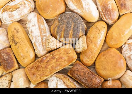 Viele Brotsorten und Brötchen, die zufällig nebeneinander auf einer hölzernen Arbeitsplatte platziert werden, als Dekoration einer traditionellen Bäckerei mit einer Mehrgenerationenorganisation Stockfoto
