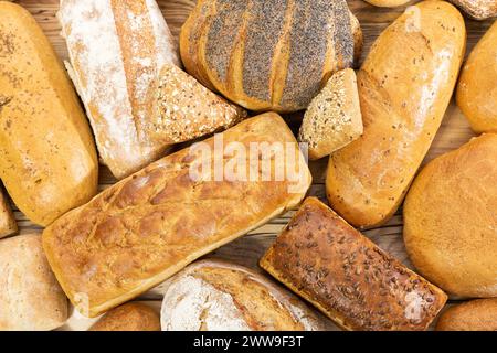 Viele Brotsorten und Brötchen, die zufällig nebeneinander auf einer hölzernen Arbeitsplatte platziert werden, als Dekoration einer traditionellen Bäckerei mit einer Mehrgenerationenorganisation Stockfoto