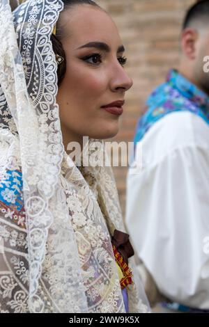 Valencianische Eleganz bei den Festlichkeiten von Gandia: Das weiße Spitzenkleid Einer Fallera, das mit traditionellen Mustern verziert ist, wird durch einen farbenfrohen Fan ergänzt Stockfoto