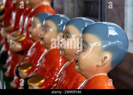 Reihe von Statuen, die Mönche im Wat Rakhang (Tempel der Glocken) in Bangkok, Thailand darstellen. In roten Gewändern, goldenen Schüsseln, rasierten Köpfen. Stockfoto