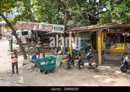 Cartagena, Kolumbien - 25. Juli 2023: Straßenecke installieren und repais Motorradschalldämpfer, wo andere Anbieter Bier und Snacks in einer Hütte verkaufen Stockfoto