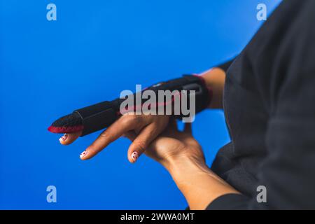 Frau zeigt eine zweiseitige Schiene auf ihrem Mittelfinger, verletzter Finger Konzept blauer Hintergrund. Hochwertige Fotos Stockfoto