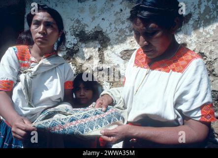 Chamula Tzotzil sprechende Maya-indische Weberinnen untersuchen die Verarbeitung und das brokadierte Design eines 100 Jahre alten Huipil (Maya-Bluse), der studiert und gefunden wurde, um ein altes Maya-Datum zu kodieren. Der alte Huipil wurde auf einem traditionellen Webstuhl mit Rückenriemen hergestellt, genau wie die Webstühle, die heute von traditionellen Maya-Webern verwendet werden. Huipils auf Late Classic (600–900 n. Chr.) Tonfiguren haben sich kaum von den heute getragenen Figuren geändert. Fotografiert am 15. November 1978 in San Juan Chamula, Highland Chiapas, Südmexiko. Stockfoto