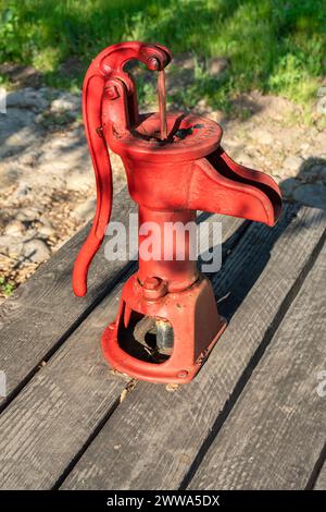 Alte rote Handwasserpumpe auf Holzdielen montiert Stockfoto