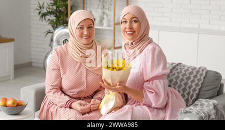 Eine muslimische Frau erhält Blumen von ihrer Tochter zu Hause. Muttertagsfeier Stockfoto