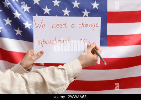 Frau, die ein Poster mit Text hält, WIR BRAUCHEN Eine ÄNDERUNG - AMTSENTHEBUNG JETZT gegen die US-Flagge Stockfoto