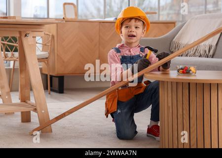 Niedlicher kleiner Baumeister, der den Nagel in eine Holzplanke im Zimmer hämmert Stockfoto