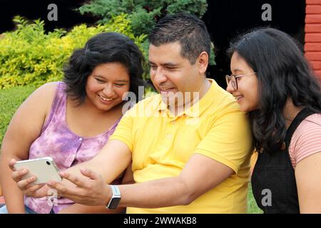 Geschiedener alleinstehender Vater mit seinen dunkelhäutigen Töchtern im Teenageralter aus Latino verbrachte Spaß mit dem Handy, um Selfies zu machen Stockfoto