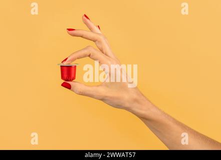 Nahaufnahme der Hand einer anonymen Frau, die rote Kaffeekapsel auf gelbem Hintergrund im Atelier hält Stockfoto
