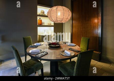 Beleuchtete Pendelleuchte über Stühlen um Holztisch mit Tellern und Weingläsern in der Restaurantecke Stockfoto