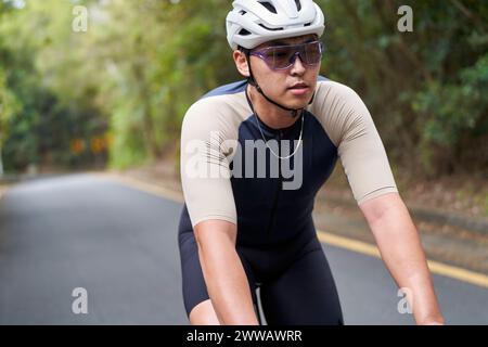 Junger asiatischer Mann, männlicher Radfahrer, der draußen auf der Landstraße Fahrrad fährt Stockfoto