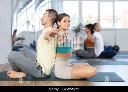 Paare Yoga-Gruppe im Studio. Ein junges Paar, das zusammen meditiert und sich Rücken an Rücken zurücklehnt. Yoga Flexibilitätsklasse Workout Stockfoto
