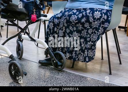Eine ältere Frau, die auf einem Stuhl sitzt, mit einem Gehhilfen an ihrer Seite. Stockfoto