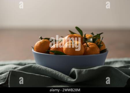 Kleine organische Mandarinen mit Blättern in Keramikschale auf Holztisch, flacher Fokus Stockfoto