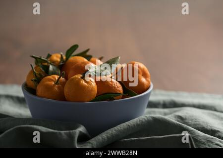 Kleine organische Mandarinen mit Blättern in Keramikschale auf Holztisch, flacher Fokus Stockfoto