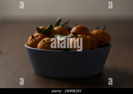 Kleine organische Mandarinen mit Blättern in Keramikschale auf Holztisch, flacher Fokus Stockfoto