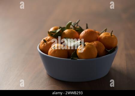 Kleine organische Mandarinen mit Blättern in Keramikschale auf Holztisch, flacher Fokus Stockfoto