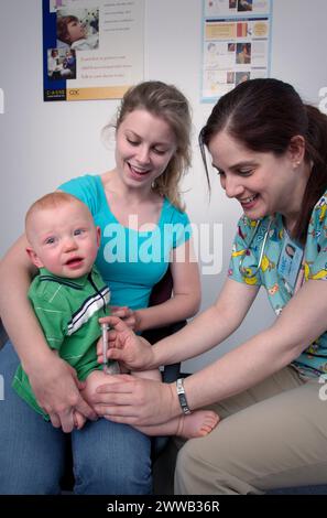 Während er auf dem Schoß seiner Mutter gehalten wurde, erhielt dieses Kind eine intramuskuläre Immunisierung in seinem rechten Oberschenkelmuskel durch eine qualifizierte Krankenschwester. Stockfoto