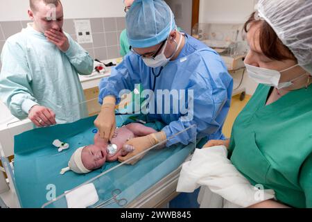 Unter dem bewegten Blick des Vaters führt ein Hebamme - Mann die ersten Untersuchungen durch, indem er die Herzfrequenz steuert. Stockfoto