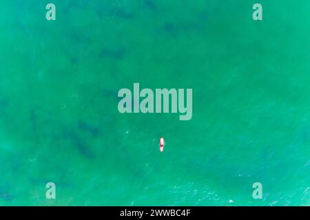 Drone aus der Vogelperspektive auf einen Surfer mit einem roten Surfbrett in einem Meer aus türkisfarbenem Wasser Stockfoto