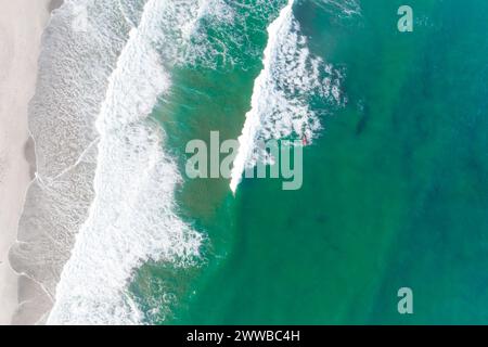 Drohnenansicht eines Surfers mit einem roten Surfbrett in einem Meer aus türkisfarbenem Wasser Stockfoto