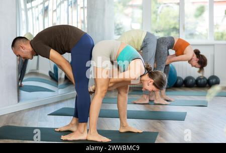 Acroyoga, zwei sportliche Menschen üben Yoga in Paaren, Paare, die Dehnübungen machen, Stehhaltung halber Vorwärtsbeugung im Yoga-Club Stockfoto