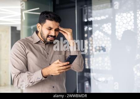 Ein Mann schaut auf sein Handy mit einem besorgten Ausdruck im Gesicht. Er hält das Telefon in der Hand und überprüft etwas Wichtiges Stockfoto