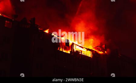 Brennendes Haus ist nachts in Flammen verwickelt. Feuer im Wohngebäude. Feuerwehrleute löschen mit Wasser. Stockfoto