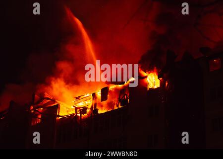 Brennendes Haus ist nachts in Flammen verwickelt. Feuer im Wohngebäude. Feuerwehrleute löschen mit Wasser. Stockfoto