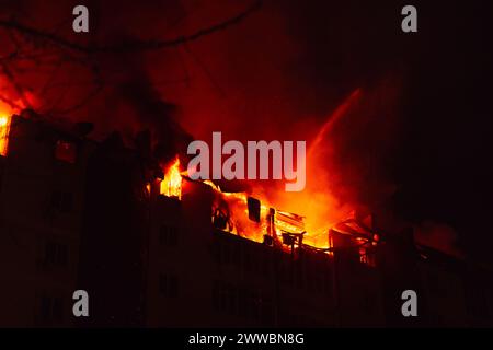 Brennendes Haus ist nachts in Flammen verwickelt. Feuerwehrleute löschen mit Wasser. Stockfoto