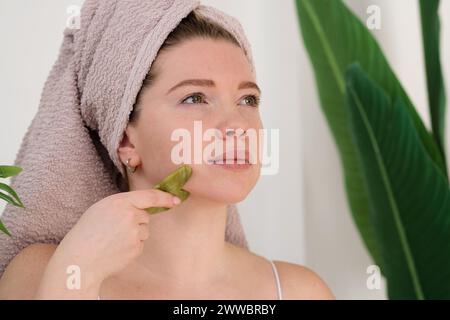 Frau, die Gesichtsmassage mit Gua-Sha-Quarzsteinkratzer durchführt. Tägliche Routine am Morgen. Stockfoto