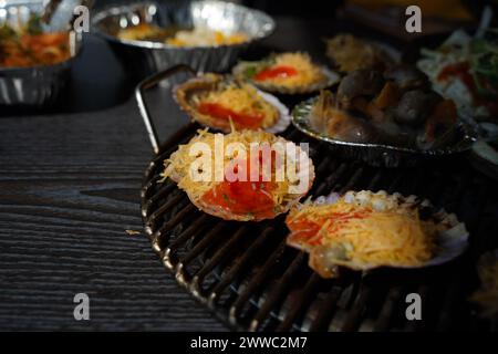 Verschiedene Arten von Muscheln werden auf einem Grill gegrillt, dann in Würze getaucht und gegessen. Stockfoto