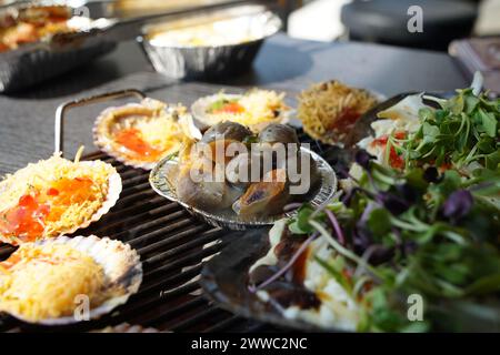 Verschiedene Arten von Muscheln werden auf einem Grill gegrillt, dann in Würze getaucht und gegessen. Stockfoto