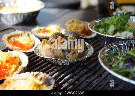 Verschiedene Arten von Muscheln werden auf einem Grill gegrillt, dann in Würze getaucht und gegessen. Stockfoto