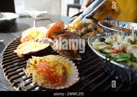 Verschiedene Arten von Muscheln werden auf einem Grill gegrillt, dann in Würze getaucht und gegessen. Stockfoto