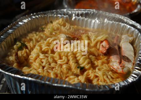 Instant-Ramen gekocht in einem Einwegbehälter aus Aluminium mit Meeresfrüchten wie Krabben Stockfoto