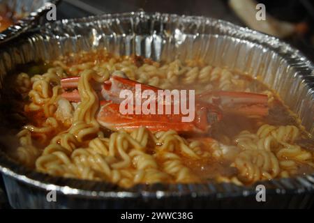 Instant-Ramen gekocht in einem Einwegbehälter aus Aluminium mit Meeresfrüchten wie Krabben Stockfoto