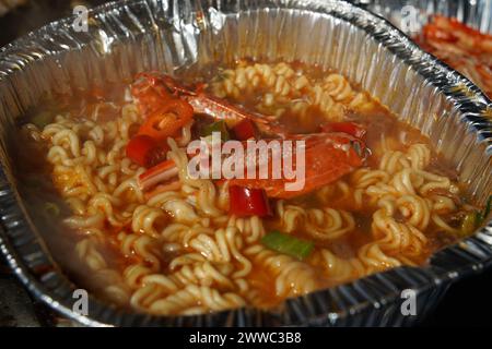 Instant-Ramen gekocht in einem Einwegbehälter aus Aluminium mit Meeresfrüchten wie Krabben Stockfoto