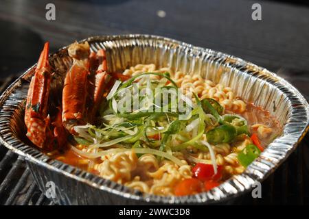 Instant-Ramen gekocht in einem Einwegbehälter aus Aluminium mit Meeresfrüchten wie Krabben Stockfoto