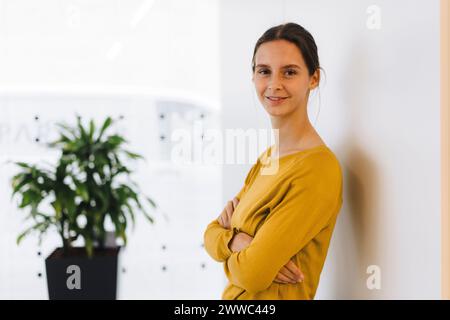 Lächelnde junge Geschäftsfrau mit überkreuzten Armen, an die Wand gelehnt Stockfoto