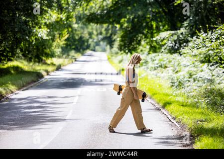 Frau, die mit Skateboard auf der Straße in der Nähe von Pflanzen im Wald läuft Stockfoto