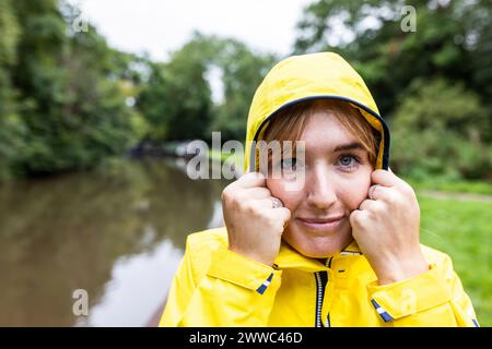 Lächelnde junge Frau mit gelbem Regenmantel im Wald Stockfoto