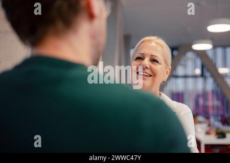 Glückliche Geschäftsfrau, die mit einem Kollegen im Amt spricht Stockfoto
