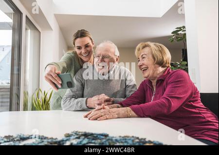 Glückliche Heim-Pflegeperson, die Selfie mit Paar am Tisch macht Stockfoto