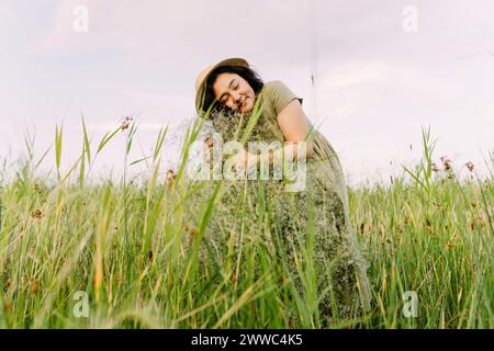 Lächelnde Frau umhüllt gypsophila-Blumen inmitten von Gras auf dem Feld Stockfoto